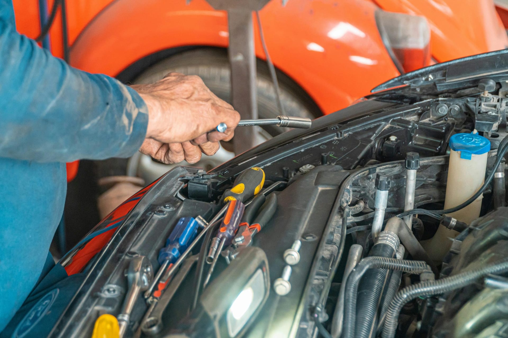Mechanic's hands using tools on a vehicle in an auto repair bay